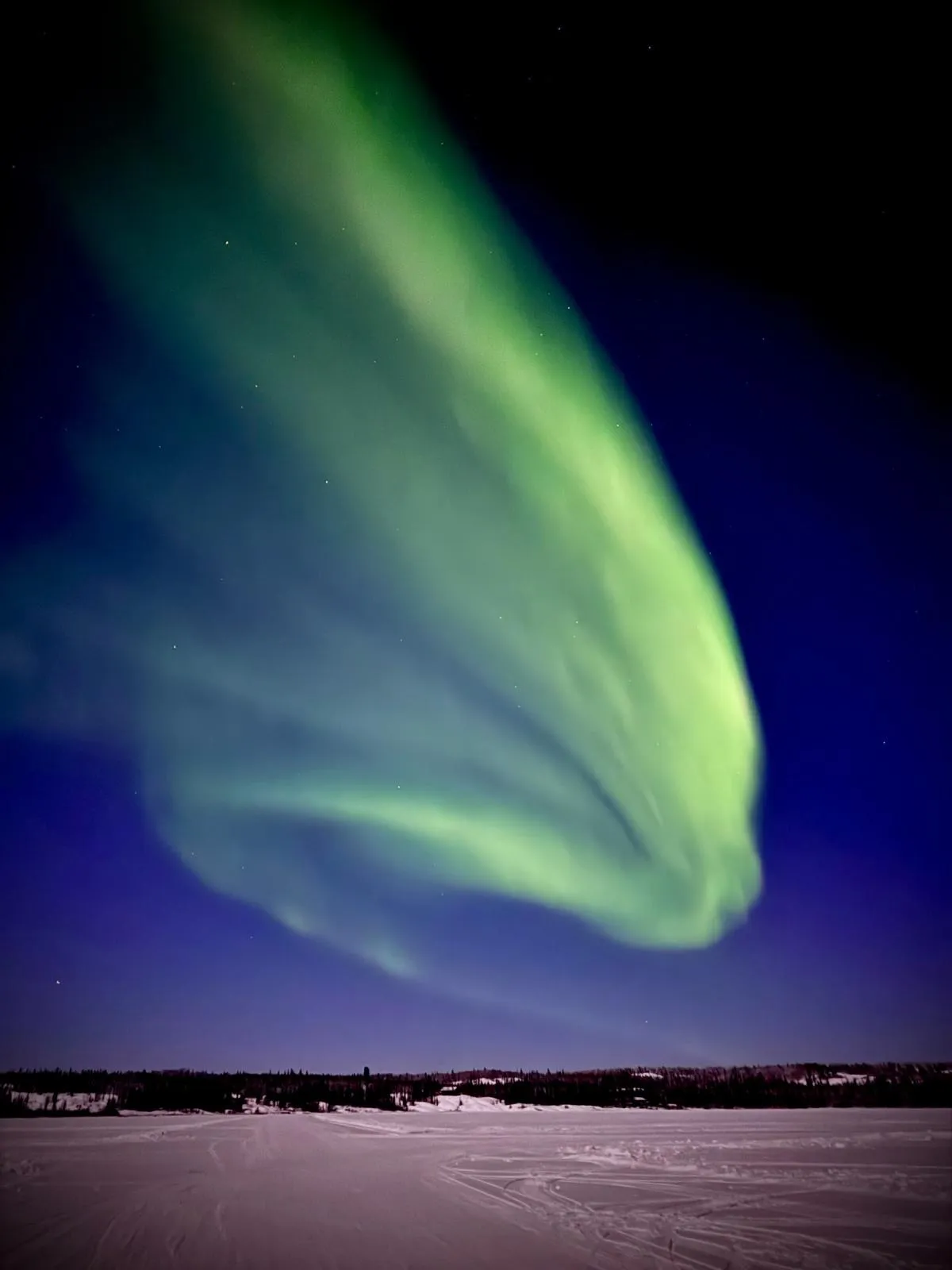 An aurora band sweeping up from a frozen lake